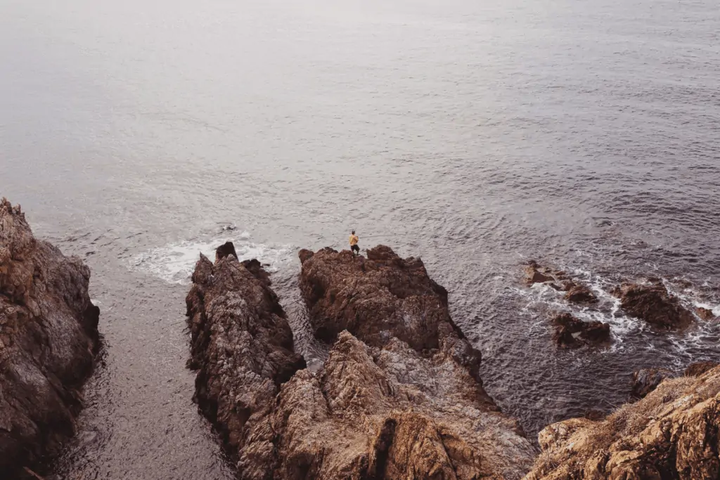 guy fishing in ocean on rocks
