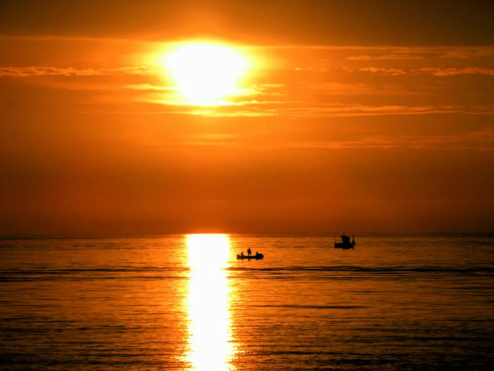 man fishing on a boat and sunset